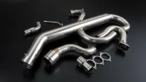 Sleek stainless steel exhaust pipe system components laid out on dark surface, showing mandrel bends and precision engineering, professional automotive photography