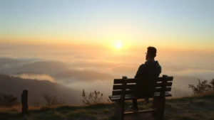 Serene person sitting peacefully on a wooden bench overlooking misty mountains at sunrise, natural landscape background, calm contemplative expression