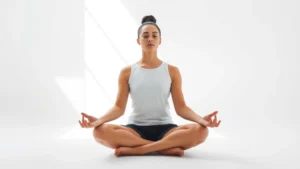 Person sitting cross-legged in peaceful meditation pose in bright natural light, focused serene expression, minimalist white background, professional photography